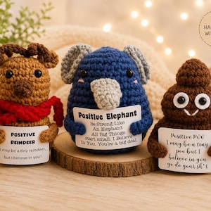 May include: Three crocheted figures: a brown reindeer with a red scarf, a blue elephant with gray ears, and a brown poop emoji. Each holds a white card with text: Positive Reindeer, Positive Elephant, and Positive Poo with motivational messages.