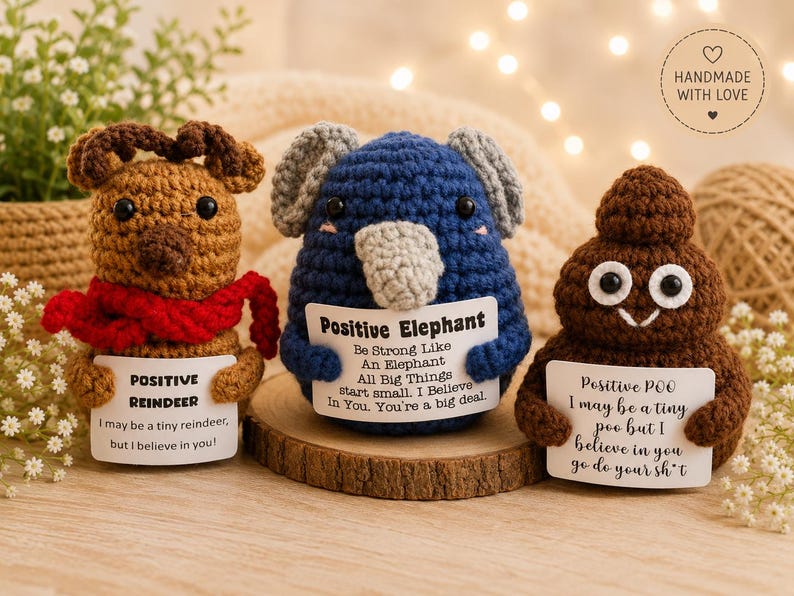 May include: Three crocheted figures: a brown reindeer with a red scarf, a blue elephant with gray ears, and a brown poop emoji. Each holds a white card with text: Positive Reindeer, Positive Elephant, and Positive Poo with motivational messages.