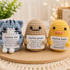 May include: Three small crochet figures: a blue striped cat, a tan potato, and a yellow duck. Each figure holds a white sign with black text. The cat sign reads Positive Cat, the potato sign reads Positive potato, and the duck sign reads Positive Duck, each with encouraging messages.