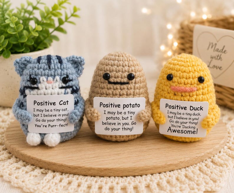 May include: Three small crochet figures: a blue striped cat, a tan potato, and a yellow duck. Each figure holds a white sign with black text. The cat sign reads Positive Cat, the potato sign reads Positive potato, and the duck sign reads Positive Duck, each with encouraging messages.