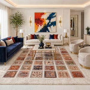 May include: A modern living room featuring a navy blue velvet sofa, a cream-colored sofa, and two beige armchairs. A large area rug with a patterned design in shades of red, orange, and blue sits in the center of the room. Abstract art decorates the walls.