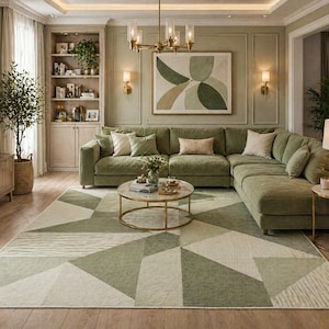 May include: A living room featuring a large, olive green sectional sofa, a geometric patterned rug in shades of green and cream, and a round coffee table. The room is decorated with a neutral color palette and includes a built-in bookcase and a framed abstract artwork.