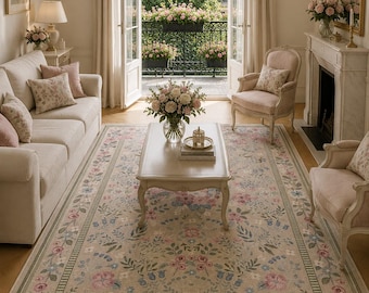 May include: A living room scene featuring a beige floral rug with pink, blue, and green accents. The room includes a white sofa, two armchairs, a coffee table, and a fireplace. A balcony with flowers is visible through open French doors.