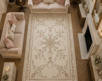 May include: An overhead view of a living room with a large floral rug, two sofas, and two armchairs in a soft pink color scheme. The rug features a cream background with pink and green floral patterns. A chandelier hangs above the seating area.