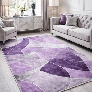 May include: A large, rectangular area rug with a geometric design in shades of purple and gray. The rug features a pattern of overlapping shapes and lines, creating a modern and stylish look. The rug is placed in a living room setting.