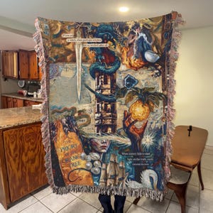 May include: A tapestry throw blanket with a detailed fantasy illustration. The artwork features a dragon, a tower, and a hand holding a glowing orb. The text "If you are a witch, then perhaps witches not so wicked after all" is visible. The blanket has fringed edges.