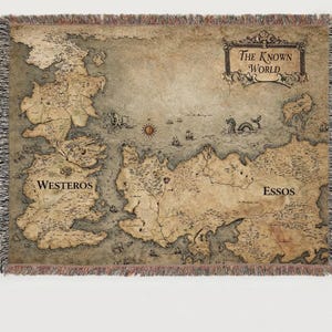 May include: A woven throw blanket featuring a map of the fictional world with the text "The Known World", "Westeros", and "Essos". The map is in shades of brown and beige, with a fringed border.