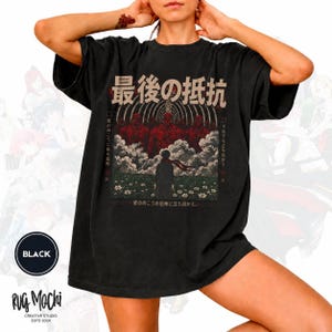 Op de afbeelding: Een zwart t-shirt met korte mouwen en een grafische print van een personage dat in een bloemenveld staat voor rode titanen en boogstructuren. Het ontwerp bevat Japanse tekst en een donkere, sfeervolle scène met wolken.