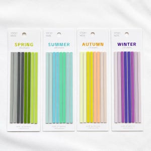 May include: Four vertical white cards, each containing 200 thin, rectangular sticky notes in color-coded sets labeled Spring, Summer, Autumn, and Winter. Each card features eight narrow adhesive strips in varying shades of green, blue, yellow, and purple.