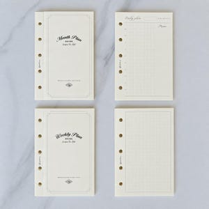 May include: Four off-white planner refill pages with six-hole punches along the left side. The pages feature black text including Month Plan, Weekly Plan, and Daily Plan, along with grid patterns, memo sections, and decorative borders.