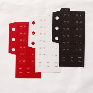 Puede incluir: Tres separadores de papel rectangulares en rojo, blanco y negro. Cada separador tiene tres orificios circulares perforados a la izquierda, números dorados del 01 al 12 y etiquetas en la parte inferior que dicen Tab, Title y Memo.