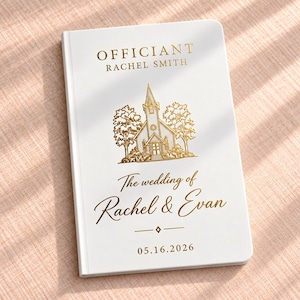 May include: A white hardcover book with gold foil lettering and a gold line art illustration of a church surrounded by trees. The text reads: OFFICIANT RACHEL SMITH, The wedding of Rachel & Evan, and the date 05.16.2026 with a small diamond icon.