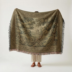 May include: A large tapestry throw blanket with a detailed forest scene in shades of green, brown, and beige. The blanket features a decorative border and fringe along the edges. The design includes trees, a bird, and a small building.