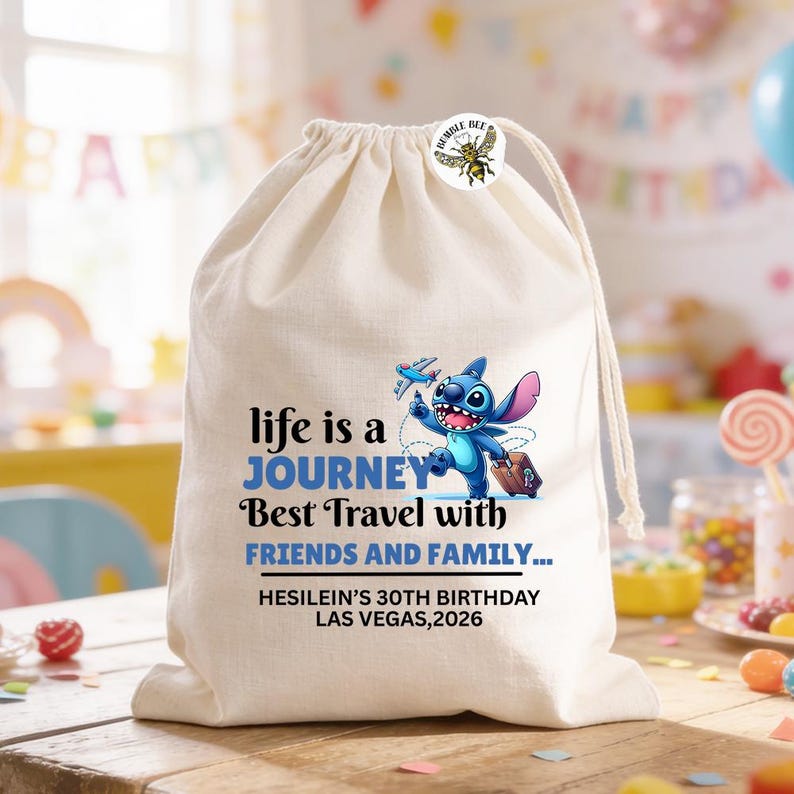 Może przedstawiać: Beżowa torba ze sznurkiem z niebieską postacią z kresk&oacute;wki z walizką i samolotem. Tekst na torbie brzmi "life is a JOURNEY Best Travel with FRIENDS AND FAMILY..." i "HESILEIN'S 30TH BIRTHDAY LAS VEGAS, 2026". Dołączona jest naklejka Bumble Bee.