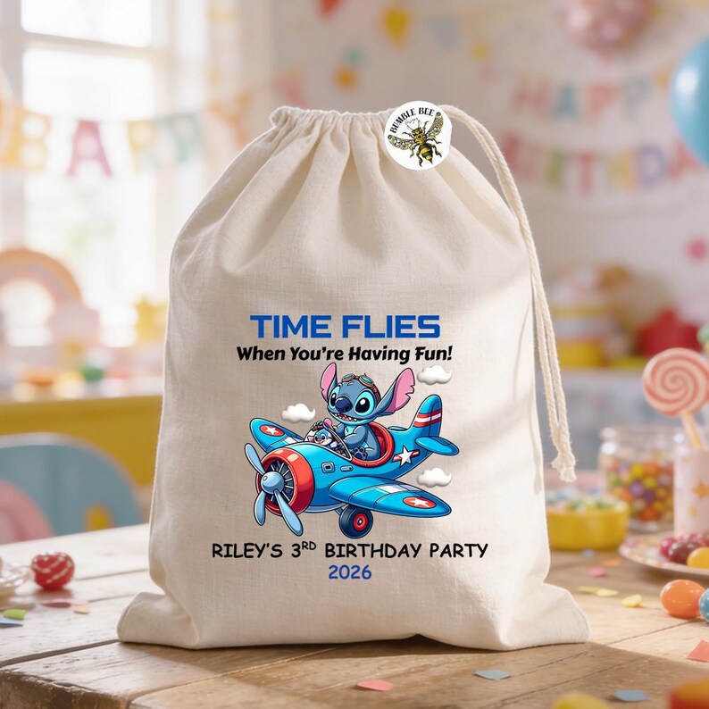 May include: A beige drawstring bag with a blue airplane graphic featuring a cartoon character. Text on the bag reads "TIME FLIES When You're Having Fun!" and "RILEY'S 3RD BIRTHDAY PARTY 2026". A Bumble Bee button is attached.