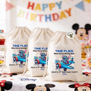 May include: Three off-white drawstring bags with a blue airplane graphic featuring a cartoon character. Text on the bags reads "TIME FLIES When You're Having Fun!" and "RILEY'S 3rd BIRTHDAY PARTY 2026". A "HAPPY BIRTHDAY" banner is in the background.