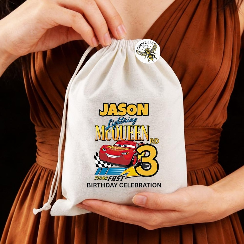Puede incluir: Una bolsa blanca con cord&oacute;n, con un dise&ntilde;o colorido de Rayo McQueen, el nombre "Jason" y el n&uacute;mero "3". El texto "Think Fast Birthday Celebration" tambi&eacute;n est&aacute; impreso. Una peque&ntilde;a pegatina redonda con una abeja est&aacute; adherida en la parte superior.