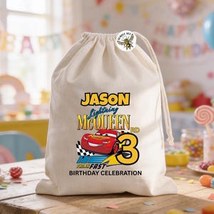 Puede incluir: Una bolsa beige con cord&oacute;n, con un dise&ntilde;o de Rayo McQueen, el nombre "Jason" y el n&uacute;mero "3". La bolsa incluye el texto "Think Fast Birthday Celebration" y un bot&oacute;n de abeja.