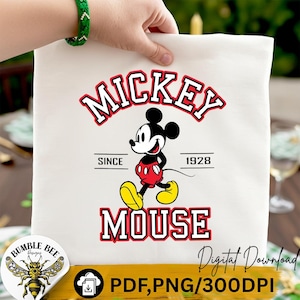 Puede incluir: Una bolsa de mano blanca con un diseño de Mickey Mouse. El diseño incluye las palabras "Mickey Mouse" en rojo y blanco, con Mickey Mouse con su atuendo icónico. También se incluye el texto "Since 1928".