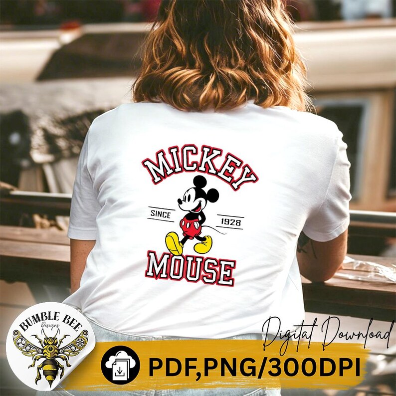 May include: White t-shirt featuring a Mickey Mouse graphic. The design includes the words "Mickey Mouse" in red and white, with Mickey Mouse in his classic pose. The text "Since 1928" is also included. The shirt has short sleeves.