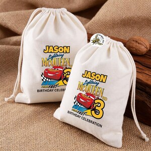 Puede incluir: Dos bolsas con cord&oacute;n de color crema con un dise&ntilde;o de Rayo McQueen. Las bolsas presentan el texto "JASON Lightning McQueen 3rd Birthday Celebration" con un gr&aacute;fico de coche de carreras rojo. Las bolsas est&aacute;n sobre una superficie texturizada.