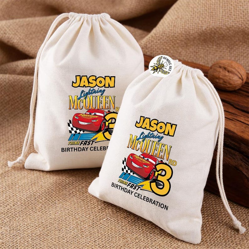 Puede incluir: Dos bolsas con cord&oacute;n de color crema con un dise&ntilde;o de Rayo McQueen. Las bolsas presentan el texto "JASON Lightning McQueen 3rd Birthday Celebration" con un gr&aacute;fico de coche de carreras rojo. Las bolsas est&aacute;n sobre una superficie texturizada.