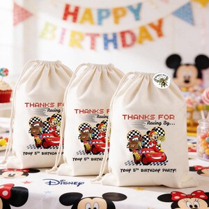 K&ouml;nnte beinhalten: Drei beige Party-Geschenkt&uuml;ten mit Kordelzug zum Thema Cars. Jede Tasche zeigt ein rotes Rennauto mit Lightning McQueen und Hook, zusammen mit dem Text "THANKS FOR Racing By..." und "TONY 5TH BIRTHDAY PARTY!"