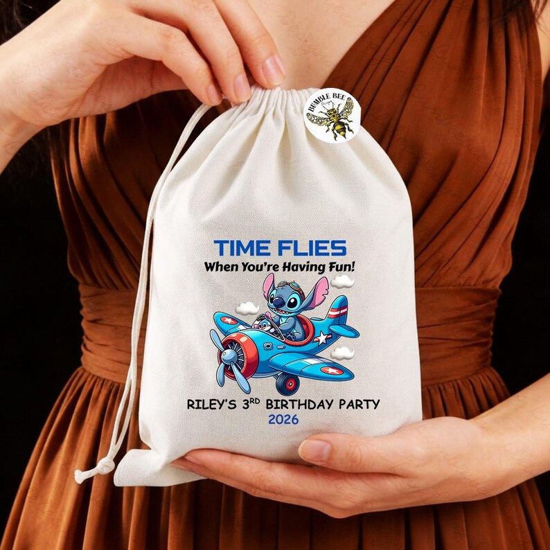 May include: A white drawstring bag featuring a cartoon image of Stitch in a blue and red airplane. The bag has the text "TIME FLIES When You're Having Fun!" and "RILEY'S 3rd BIRTHDAY PARTY 2026". A "Humble Bee" button is attached.