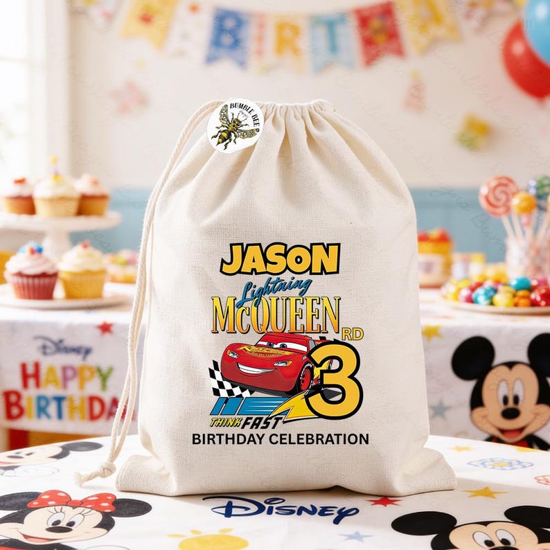 Puede incluir: Una bolsa beige con cord&oacute;n con un dise&ntilde;o de Lightning McQueen y el texto "Jason Lightning McQueen RD 3 Think Fast Birthday Celebration". Una pegatina de abeja est&aacute; en la parte superior de la bolsa. La bolsa est&aacute; sobre una mesa con cupcakes y una pancarta de Disney Happy Birthday.