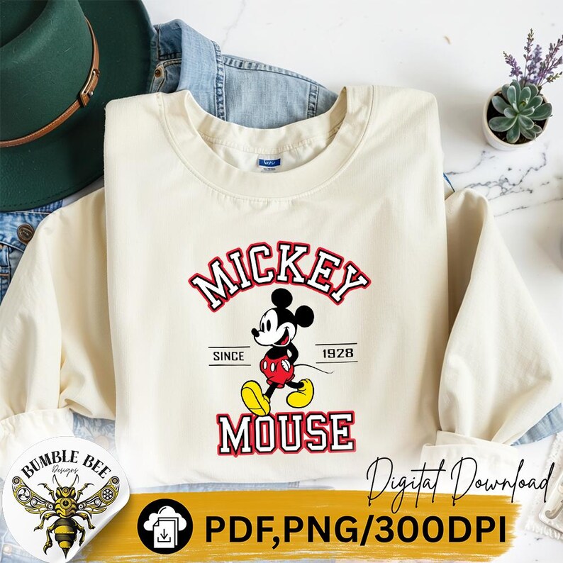 May include: Cream-colored sweatshirt featuring a Mickey Mouse graphic. The design includes the word "Mickey" in red and white, the character illustration, and the word "Mouse". The text "Since 1928" is also included.