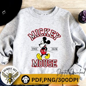 May include: A light gray sweatshirt featuring a graphic of Mickey Mouse. The design includes the words "Mickey Mouse" in red and white, with "Since 1928" below. The cartoon character is depicted in his classic outfit.