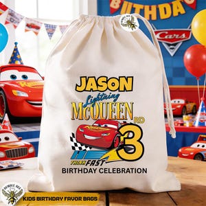 Puede incluir: Una bolsa de regalo con cord&oacute;n de color crema con Lightning McQueen de la pel&iacute;cula Cars. La bolsa tiene el nombre "Jason", el n&uacute;mero "3" y el texto "Birthday Celebration". La bolsa est&aacute; decorada con una bandera a cuadros.