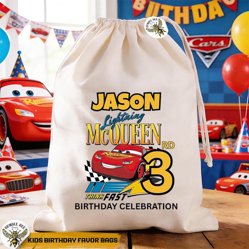 Puede incluir: Una bolsa de regalo con cord&oacute;n de color crema con Lightning McQueen de la pel&iacute;cula Cars. La bolsa tiene el nombre "Jason", el n&uacute;mero "3" y el texto "Birthday Celebration". La bolsa est&aacute; decorada con una bandera a cuadros.