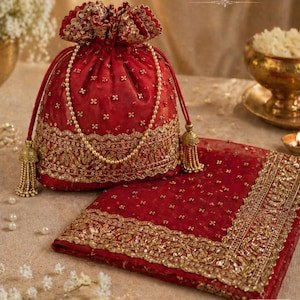 Könnte beinhalten: Ein rotes Dupatta- und Potli-Set. Die Potli-Tasche ist mit goldener Stickerei und einer Perlenkette verziert. Das passende Dupatta weist aufwendige goldene Details an den Rändern auf. Das Set wird auf einer neutralen Oberfläche präsentiert.