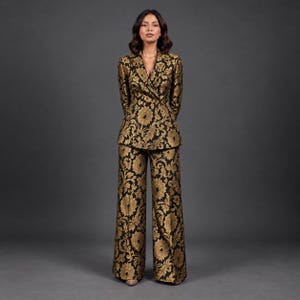 May include: A two-piece suit comprising a double-breasted blazer and wide-leg trousers. The garment features a black base fabric with a prominent gold floral brocade pattern throughout, including long sleeves, a notched lapel, and a tailored fit.