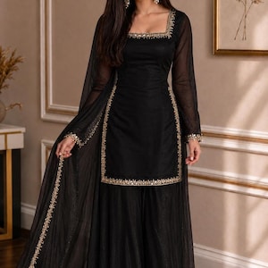 May include: A black three-piece ensemble featuring a long-sleeved tunic with a square neckline, wide-leg trousers, and a matching sheer dupatta. The tunic and dupatta are adorned with intricate gold embroidery along the edges and cuffs.