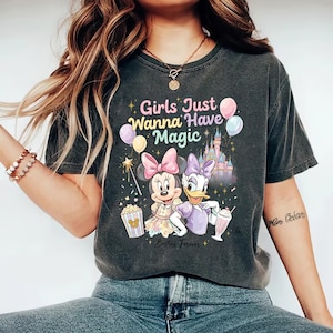May include: Dark gray t-shirt featuring Minnie Mouse and Daisy Duck with the text "Girls Just Wanna Have Magic" and "Besties Forever." The graphic includes a castle, balloons, popcorn, and a milkshake.