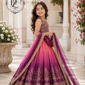 May include: A sleeveless lehenga choli featuring a bodice with intricate embroidery and a floor-length skirt with a pink to purple ombre gradient. The skirt is adorned with gold floral embroidery and a wide border, paired with a sheer purple dupatta.