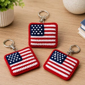 May include: Three square crochet keychains featuring the American flag design with red and white horizontal stripes and a blue canton with white stars. Each keychain is attached to a silver-toned metal split ring with a lobster claw clasp.