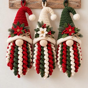 May include: Three hanging crochet gnome ornaments with pointed hats in red, cream, and dark green. Each gnome features a round nose, a long beard made of spiraled yarn in red, cream, and green, and a decorative floral accent with berries.