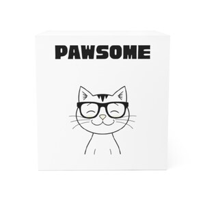 May include: White square block featuring the word "PAWSOME" in black capital letters. Below the text is a black and white cartoon cat wearing glasses and smiling.