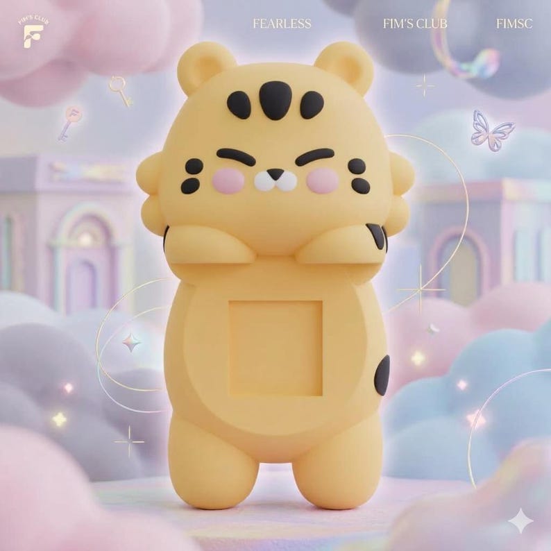 May include: A yellow tiger-shaped phone stand with black markings on the ears, forehead, and sides. The character has pink cheeks, a small nose, and a square cutout in the center of its torso. The text FEARLESS, FIM'S CLUB, and FIMSC appear above.