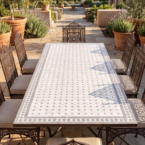 Può includere: Un tavolo da pranzo rettangolare con piano piastrellato geometrico bianco e grigio e struttura in metallo scuro, circondato da otto sedie in metallo abbinate con schienali traforati complessi e cuscini di seduta color beige chiaro.
