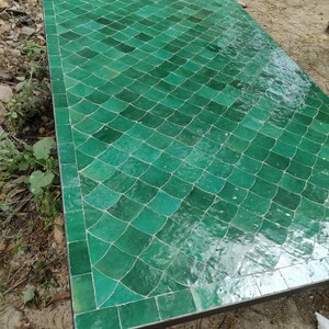 Könnte beinhalten: Eine rechteckige Tischplatte mit einem Mosaikmuster aus glänzenden, smaragdgrünen Fliesen, die in einem sich wiederholenden Fischschuppen- oder Fächermuster angeordnet sind. Die Oberfläche besteht aus vielen kleinen, handgefertigten Keramikstücken.