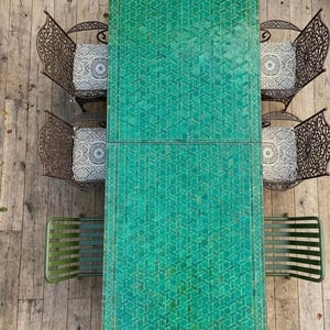 May include: An overhead view of an outdoor dining set. A rectangular green mosaic tile table is surrounded by six chairs. Two chairs have ornate metal backs and patterned cushions. The other four chairs are green metal with slat backs.