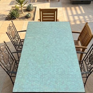 Peut inclure: Ensemble de salle à manger d'extérieur avec une table rectangulaire au plateau vert clair en mosaïque. La table est entourée de quatre chaises en fer forgé ornées et de deux chaises en bois. L'ensemble est sur un patio en pierre avec des plantes et un foyer.