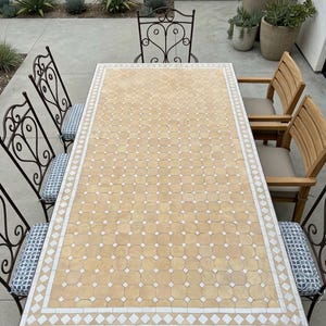 May include: An outdoor dining set featuring a rectangular table with a mosaic tile top in shades of beige and white. The table is surrounded by wrought iron chairs with patterned cushions and wooden chairs with beige cushions. The set is ideal for patio dining.