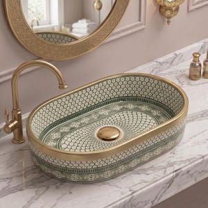 May include: An oval ceramic bathroom sink with a gold-colored rim and faucet. The sink features a white and green patterned design. The faucet and drain are also gold-colored. The sink is set on a marble countertop.