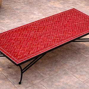 May include: A rectangular coffee table with a red tile top and a black metal frame. The tile pattern is a repeating herringbone design. The table is approximately 48 inches long and 24 inches wide.