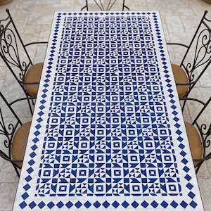 Könnte beinhalten: Rechteckiger Esstisch für den Außenbereich mit einer blau-weißen geometrischen Fliesenoberfläche. Der Tisch ist von vier schmiedeeisernen Stühlen mit braunen Sitzkissen umgeben. Das Design des Tisches zeigt ein sich wiederholendes Muster aus Quadraten, Dreiecken und Rauten.